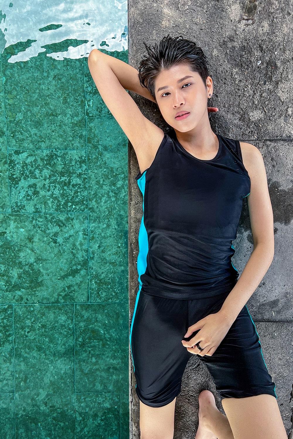 A non-binary androgynous tomboy, transgender man wearing a black color of a bandage TOMSCOUT Swimming Chest Binder to fight body dysphoria and swimming in the pool, TOMSCOUT SAPPHIRE SWIMMING BINDER.