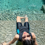 A non-binary androgynous tomboy, transgender man wearing a black color of a bandage TOMSCOUT Swimming Chest Binder to fight body dysphoria and swimming in the pool, TOMSCOUT SAPPHIRE SWIMMING BINDER.