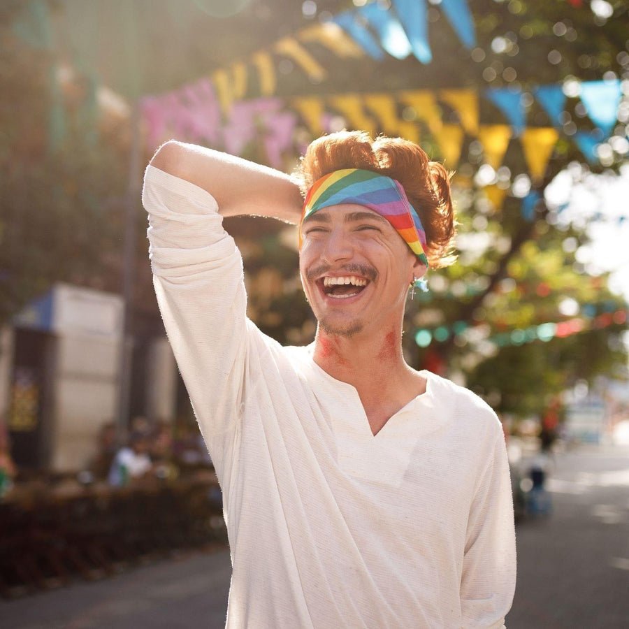 A young male smiling and wearing a LGBT rainbow pride bandana on the street, TOMSCOUT PRIDE BANDANA.