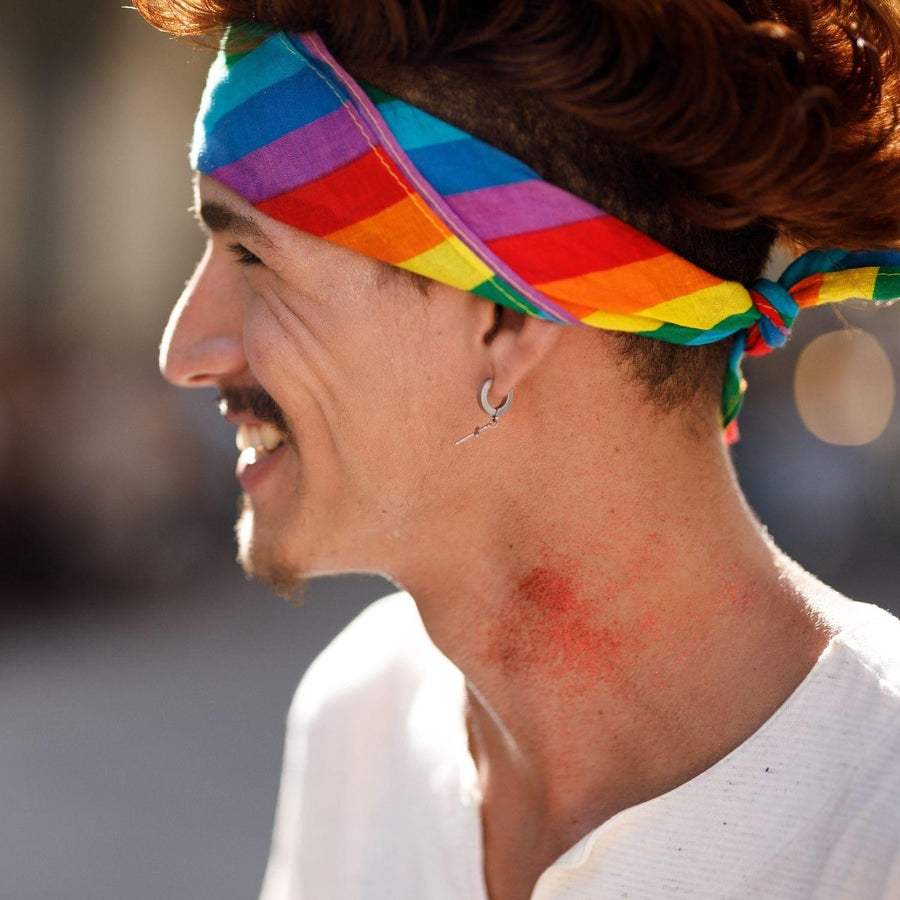 A young male smiling and wearing a LGBT rainbow pride bandana on the street, TOMSCOUT PRIDE BANDANA.