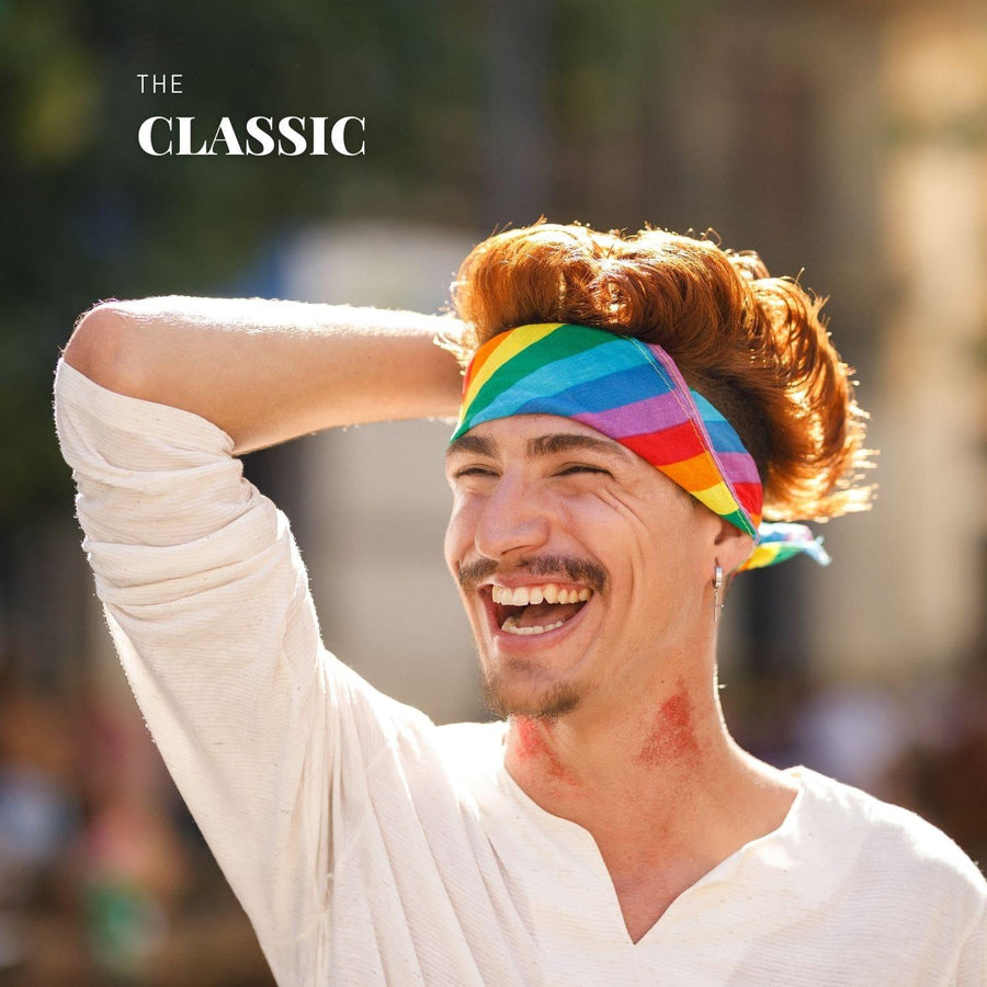 A young male smiling and wearing a LGBT rainbow pride bandana on the street, TOMSCOUT PRIDE BANDANA.
