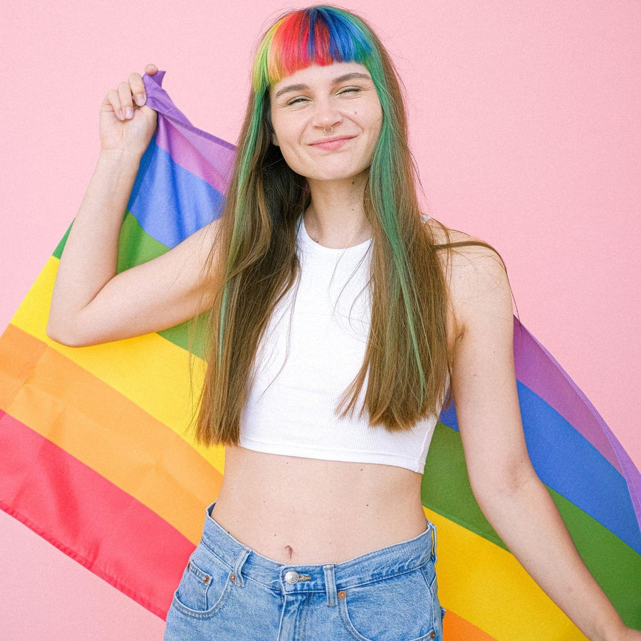 A young girl with colorful hair smiling and holding with a LGBTQ Rainbow Pride Flag, TOMSCOUT PRIDE  RAINBOW FLAG.