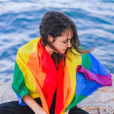 A young woman draped in an LGBTQ Rainbow Pride Flag, symbolizing protection and pride, from the TOMSCOUT LGBTQ+ Classic Pride Flag collection