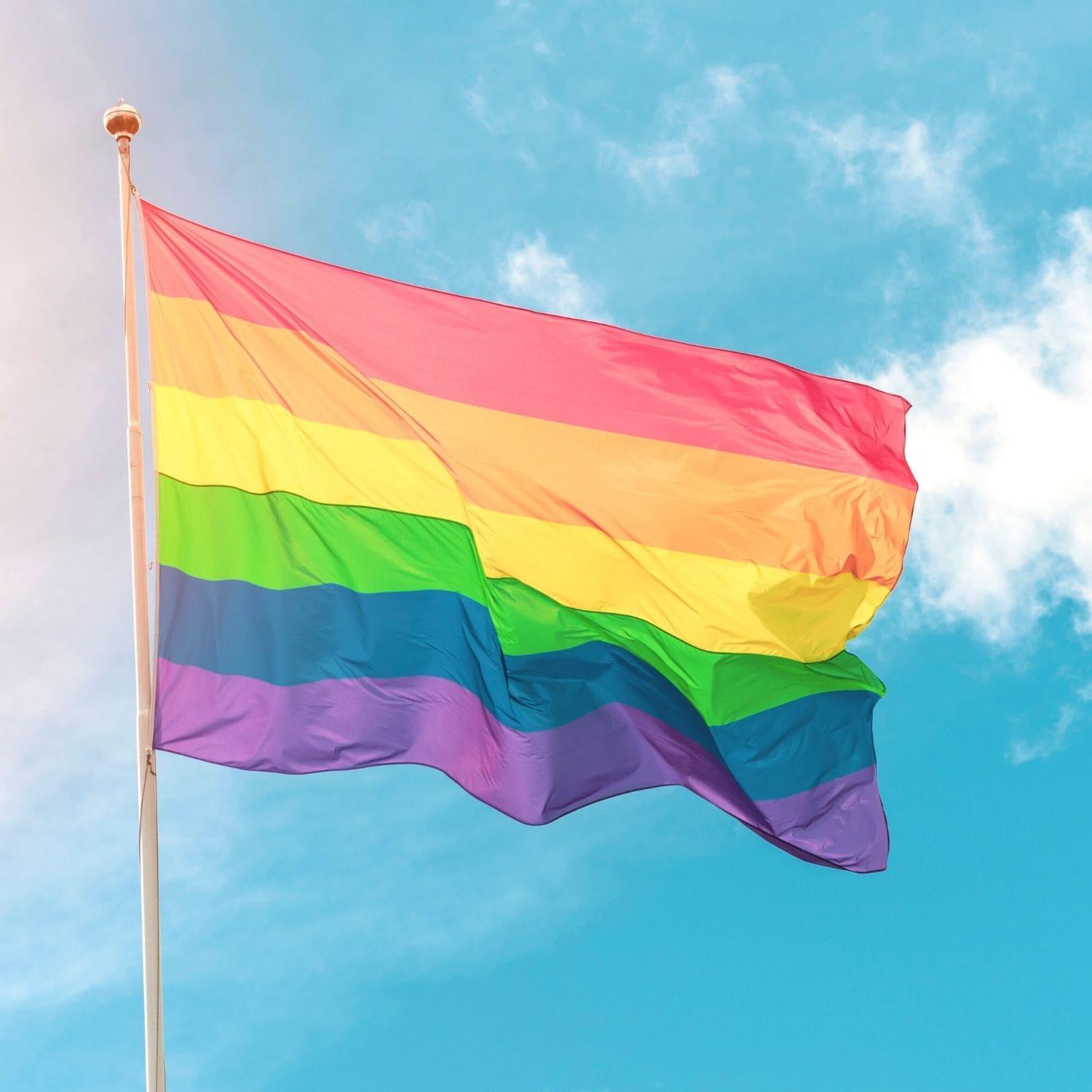 Vibrant image of a colorful LGBTQ Rainbow Pride Flag waving against the sky, part of the TOMSCOUT LGBTQ+ Classic Pride Flag collection.